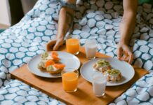 여행중에도 건강관리 하기 person serving pastries on white ceramic plates with fruit juice glasses on wooden tray on top of bed