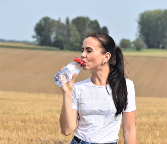 생명체에 중요한 물의 역할 a woman standing in a field drinking from a bottle